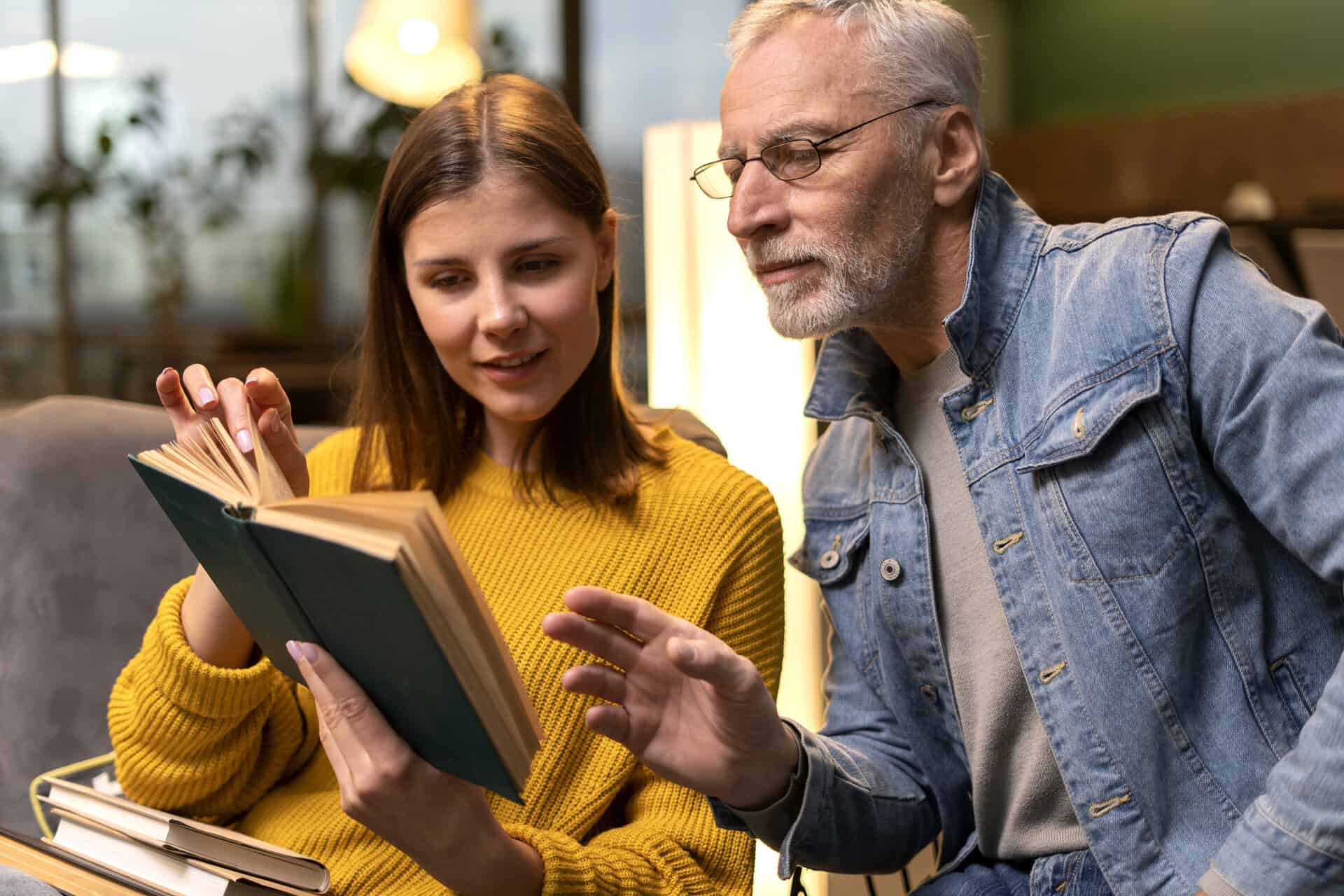A woman holds a book by the School of Evangelism and speaks as a man listens in a warm, home-like setting.