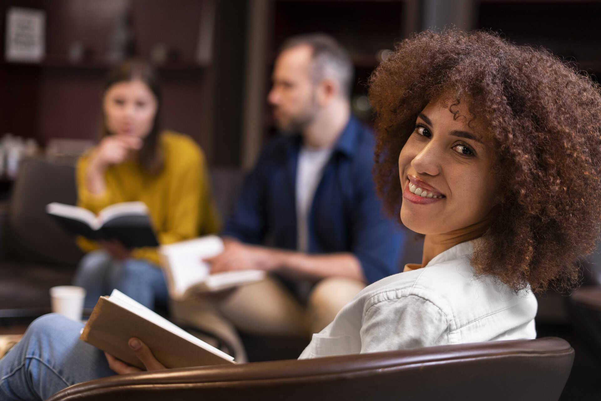 woman sitting in chair, looking up from reading her book facing the camera and smiling